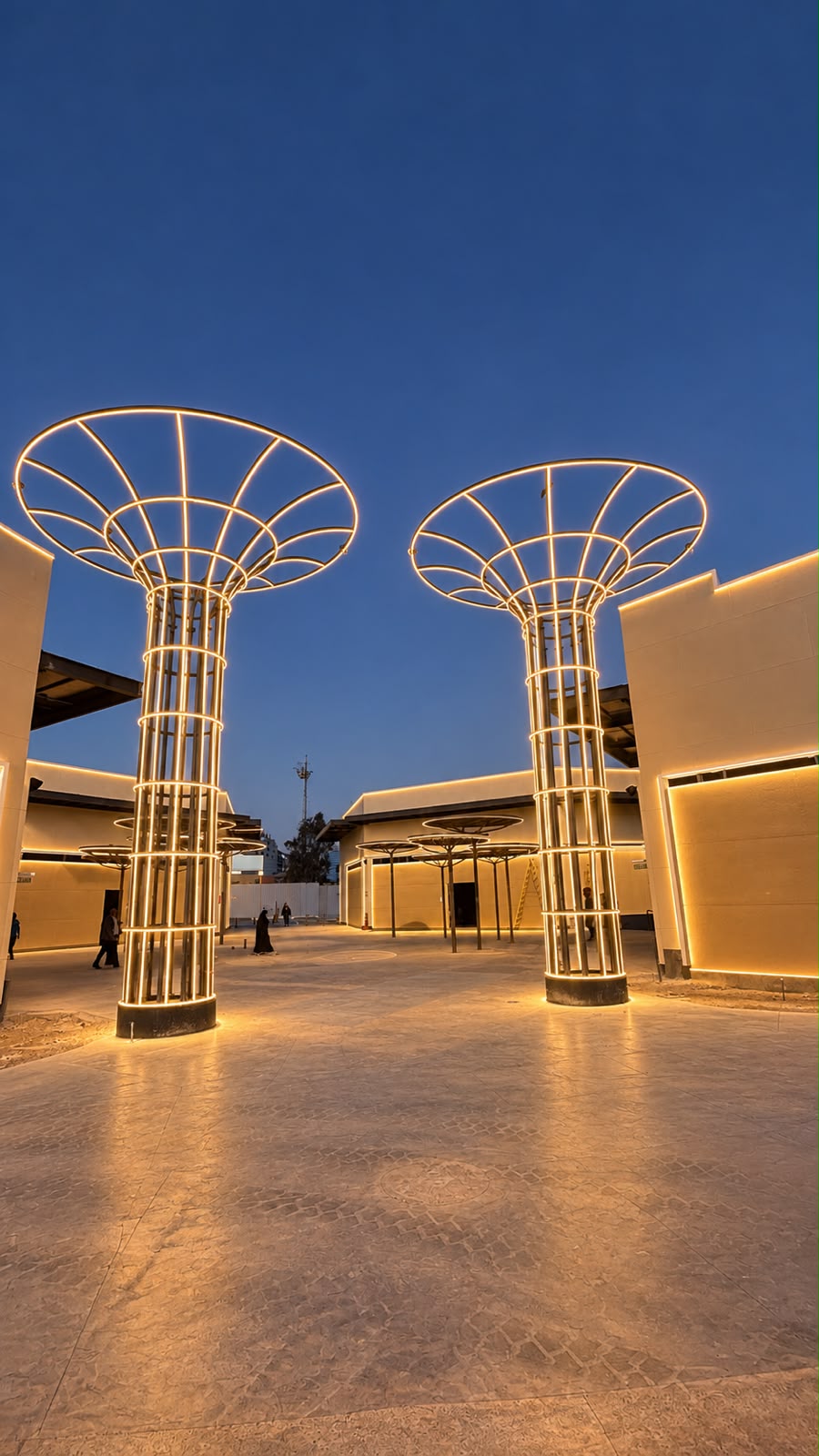 Fotografía de referencia: dos estructuras de columnas y coronas con delineado luminoso continuo en una plaza